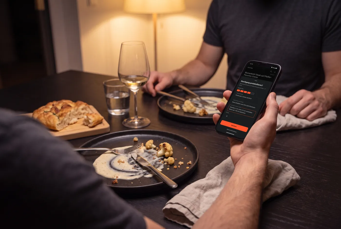 Nach dem Essen am Tisch: Eine Hand hält das Handy mit dem Kochprotokoll von Cook & Repeat über den leeren Tellern.
